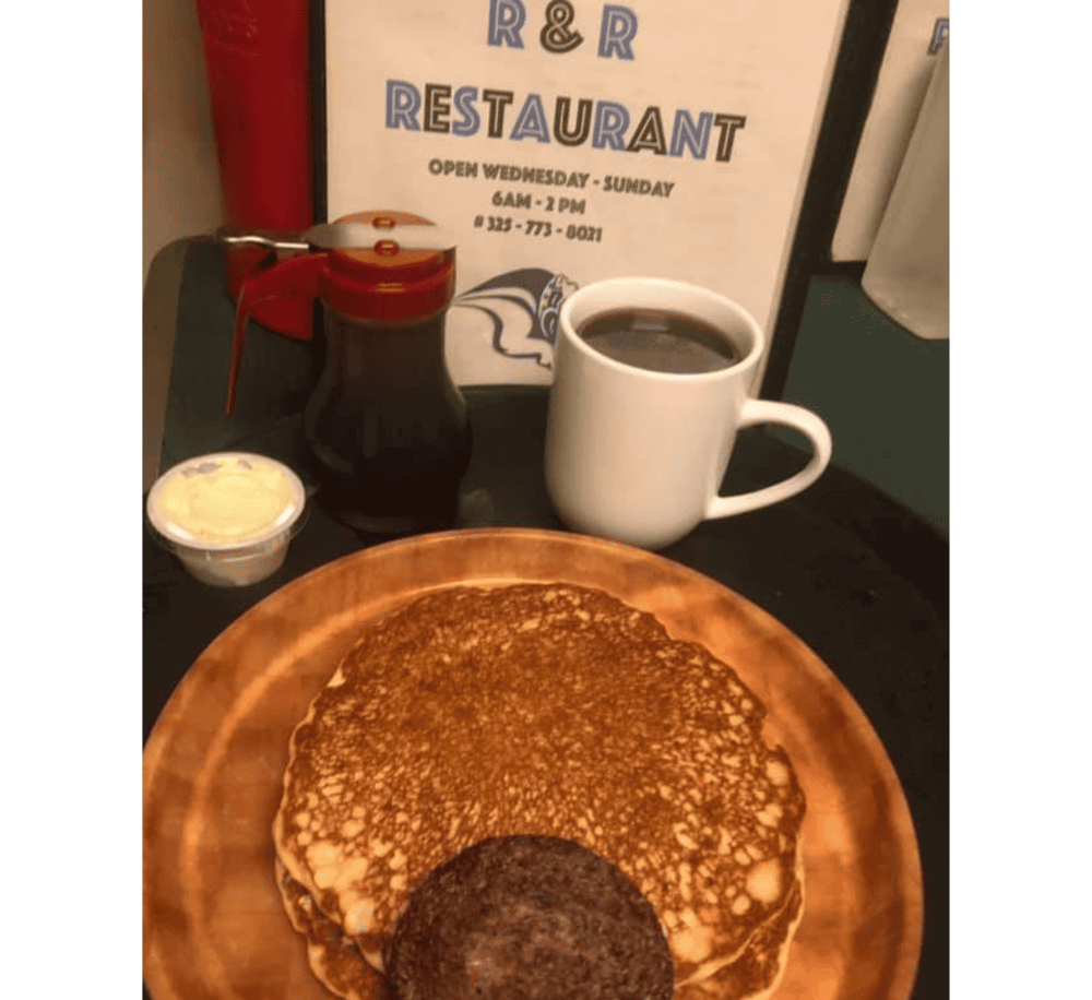 Buttermilk pancakes with a cookie, coffee, and syrup on a tray at Quest For Directions restaurant.