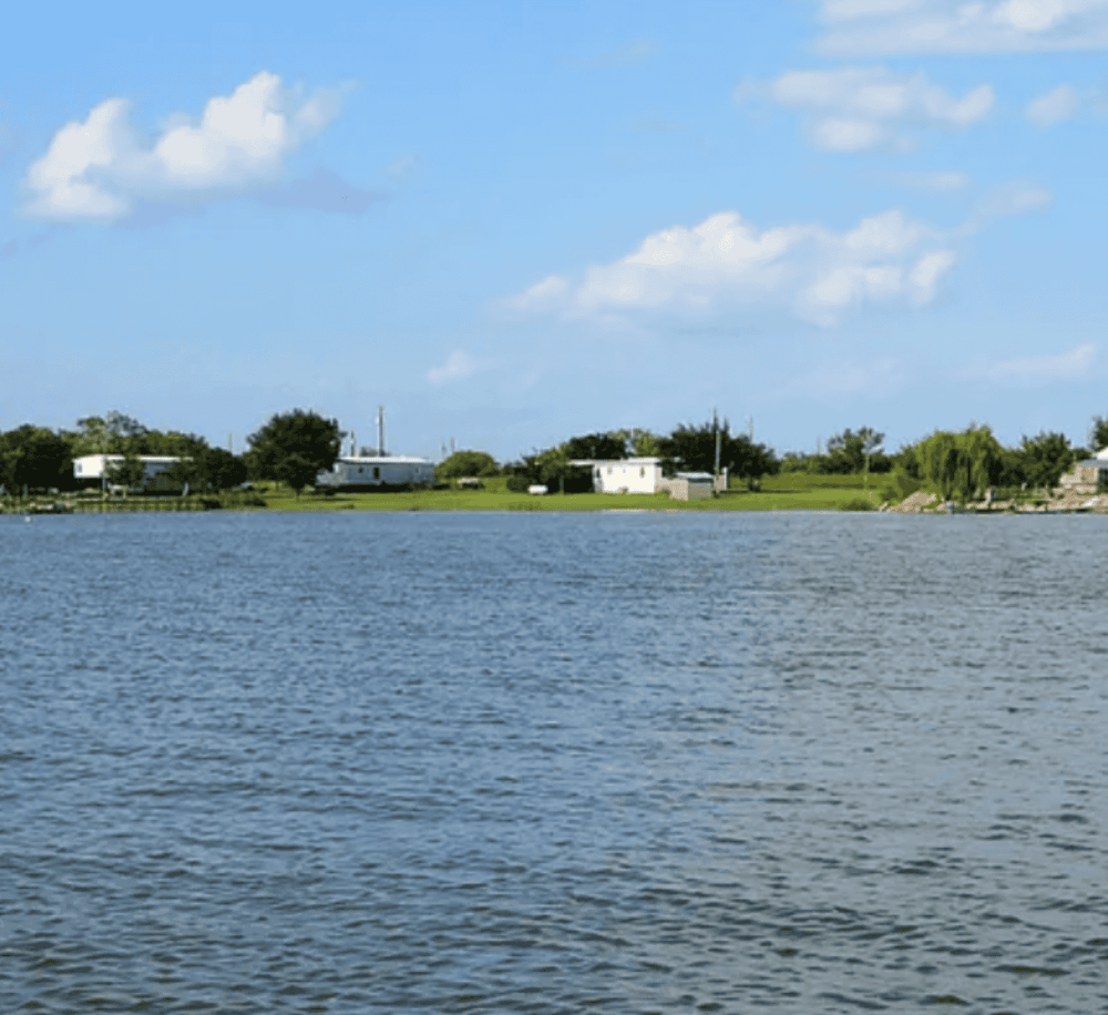 Serene lakeside view with houses, trees, and blue sky, perfect for outdoor directions and travel planning.