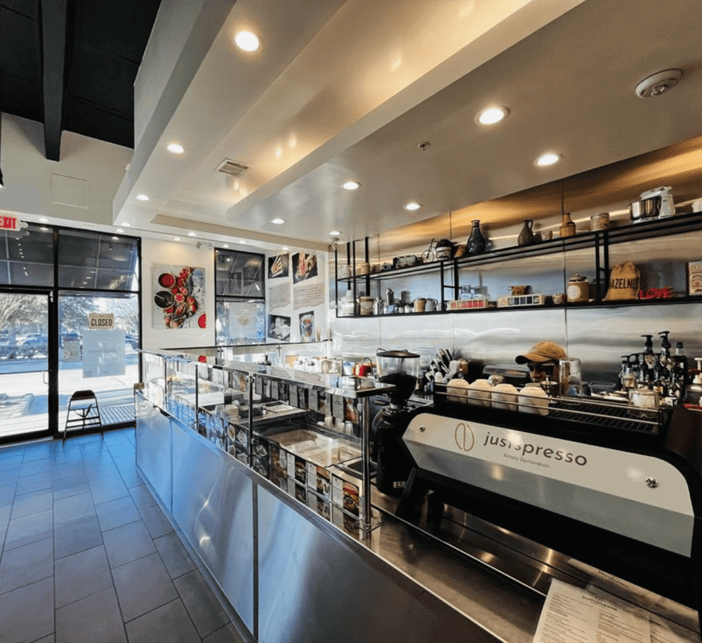 Bright modern coffee shop interior with stainless steel counter and coffee brewing equipment.