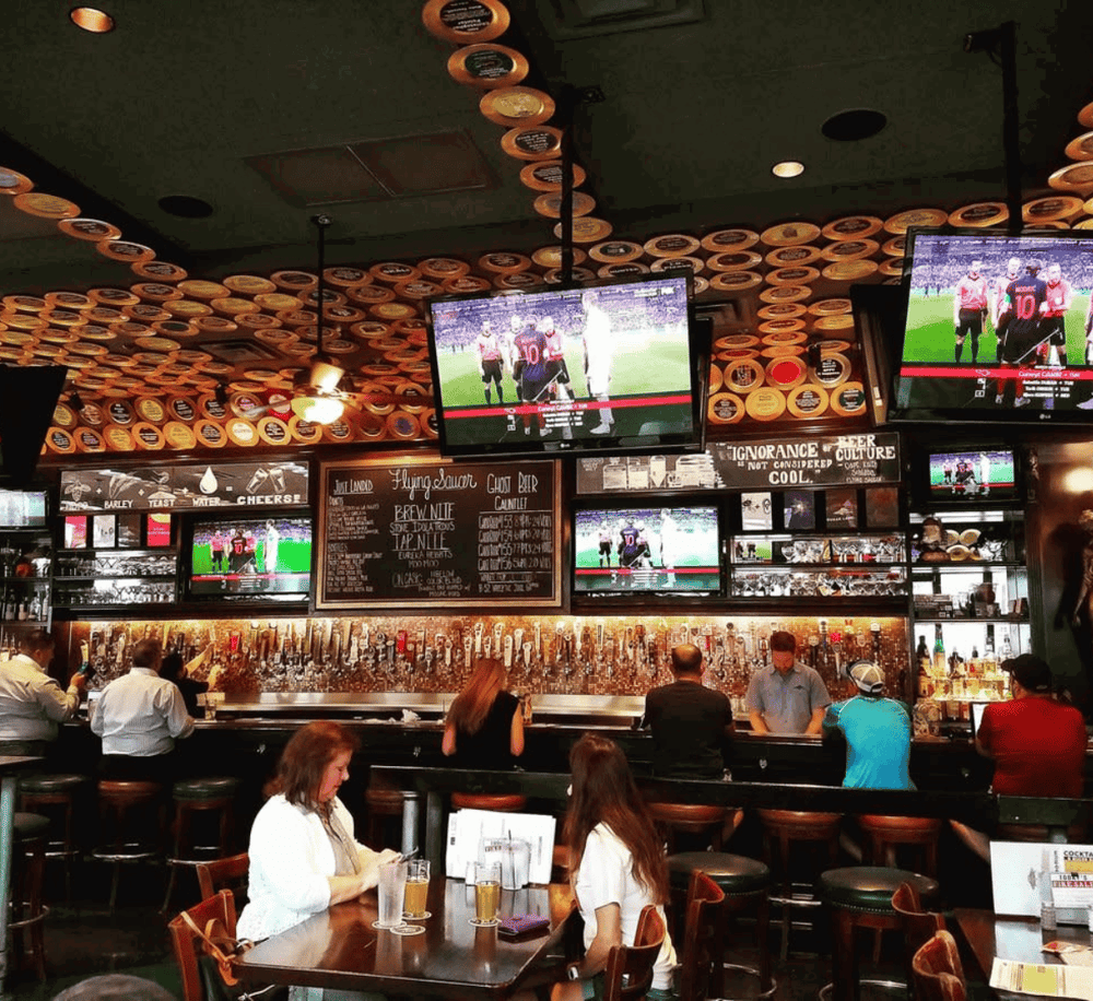 TV screens showing sports at a lively bar with patrons enjoying drinks and socializing.