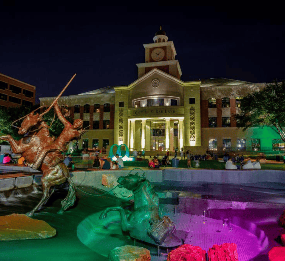 Vibrant nighttime scene at Sugar Land City Hall with illuminated sculptures and crowd, showcasing local attractions and city nightlife.