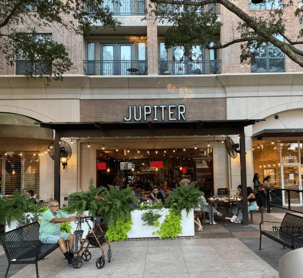Enjoy dining at Jupiter restaurant with outdoor seating and greenery in a vibrant, accessible urban setting.