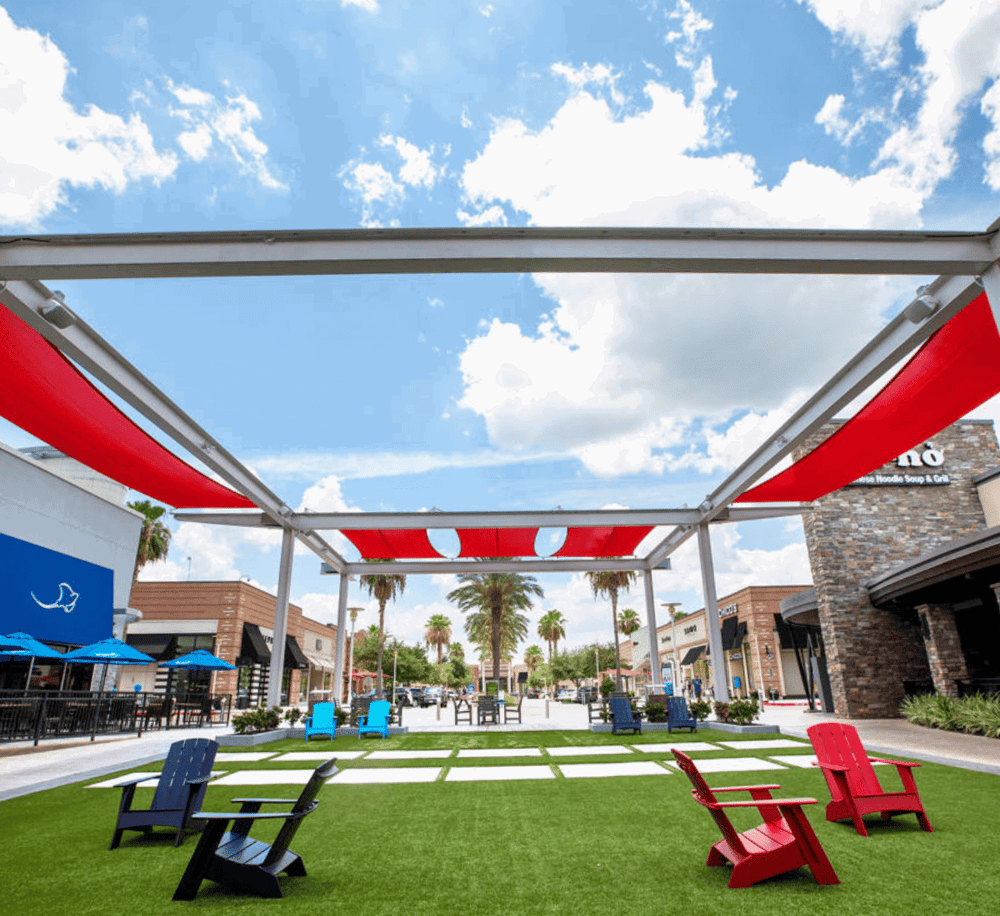 Relaxing outdoor shopping plaza with colorful chairs, modern storefronts, and sunny sky.