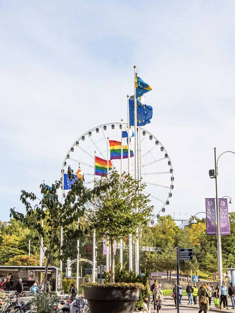 Colorful flags and a Ferris wheel at a vibrant outdoor city park.
