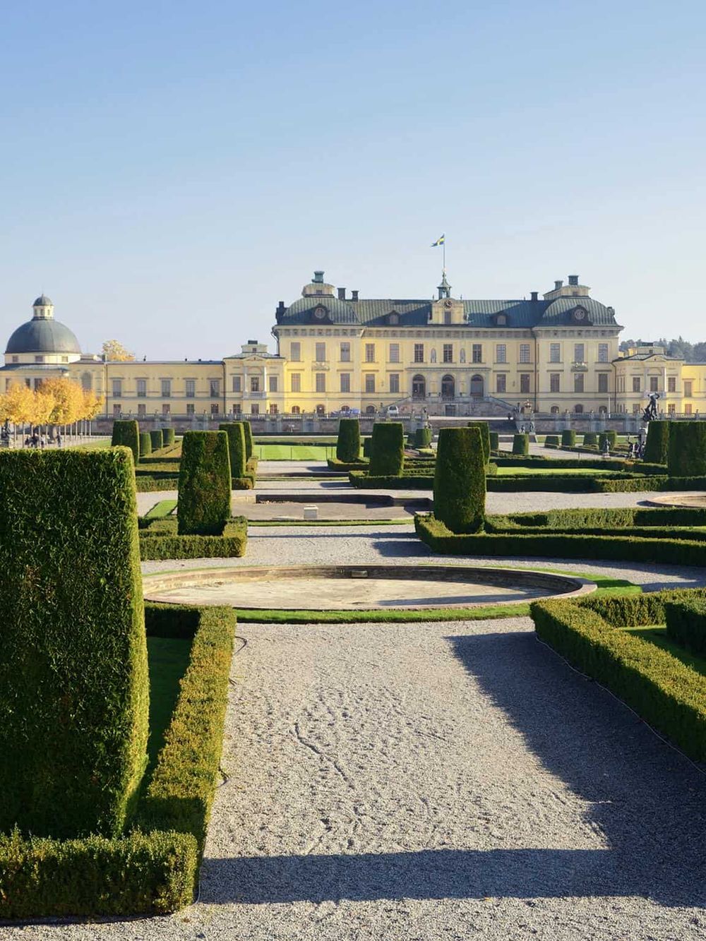 Impressive Swedish royal palace with manicured gardens in front, elegant architecture, and clear blue sky in the background.