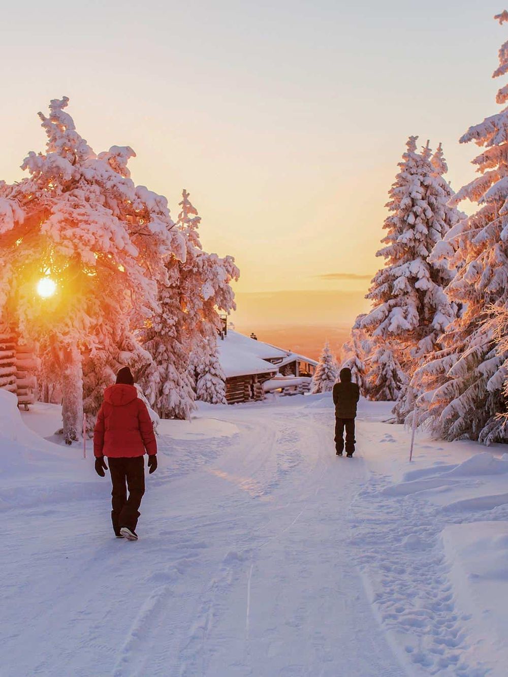 Snowy winter landscape with people walking through a forest at sunset, promoting winter travel and adventure.