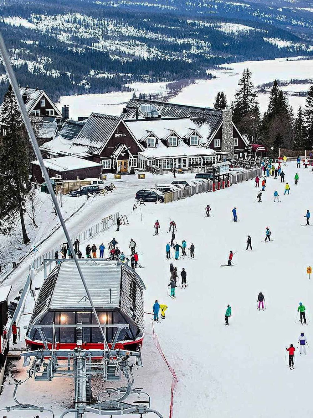 Ski resort with a ski lift, snowy slopes, and people enjoying winter sports in a scenic mountain setting.