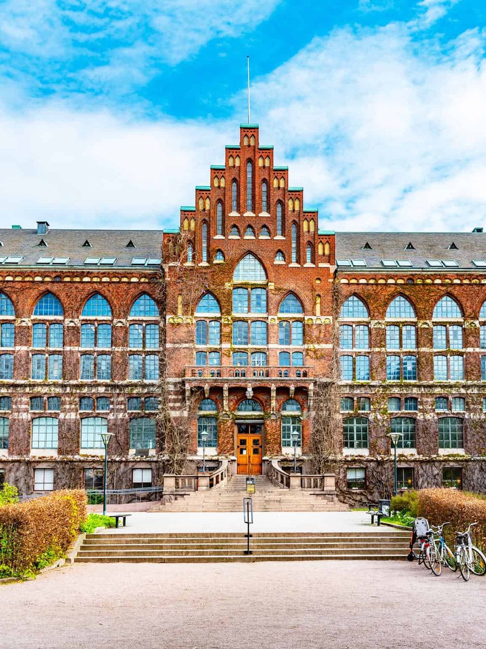 Historic brick university building with Gothic architecture, set against a bright blue sky.