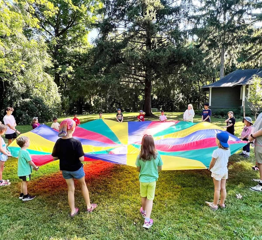Colorful parachute game with children outdoors in a lush green park setting, perfect for kids' recreational activities.