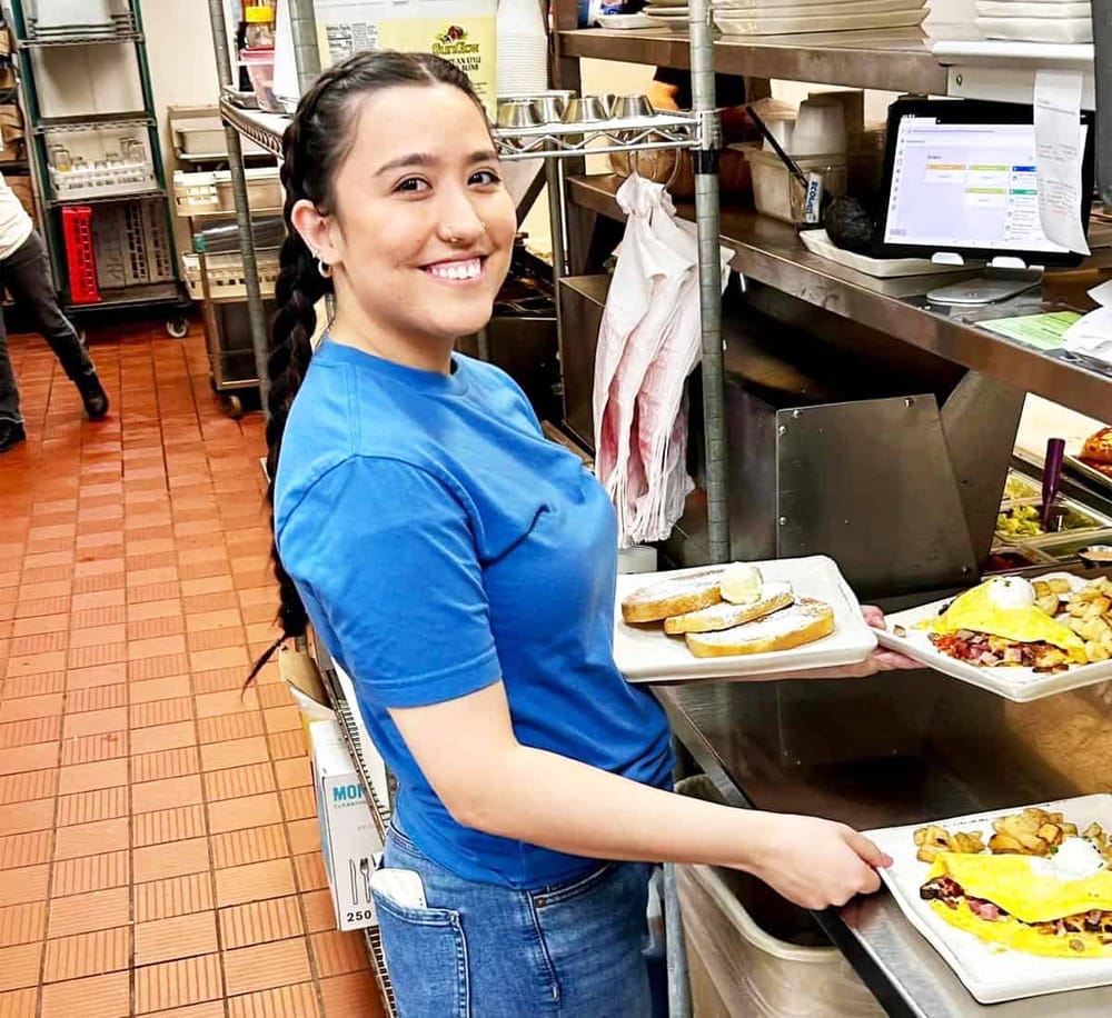 Fresh-faced young woman serving breakfast at a busy restaurant kitchen.