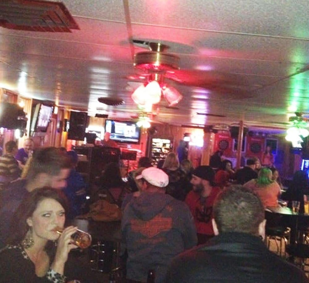 A lively bar scene with guests enjoying drinks, dim lighting, and colorful neon illumination.