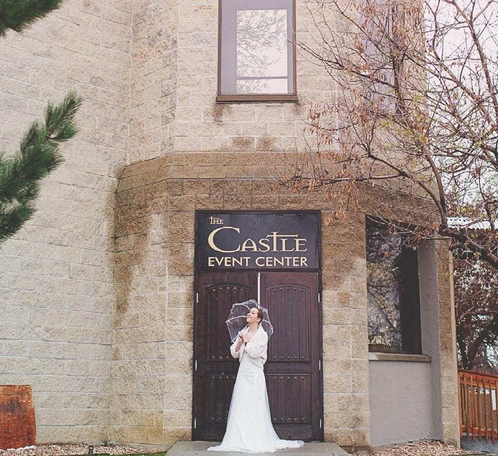 Elegant bride standing outside The Castle Event Center, stylish wedding venue with brick exterior, perfect for special occasions.