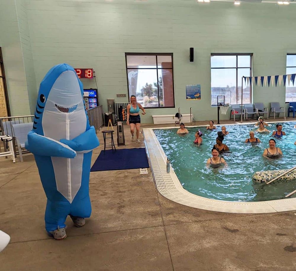 Playful shark mascot entertaining guests at indoor swimming pool event, fun family activity, Quest For Directions.
