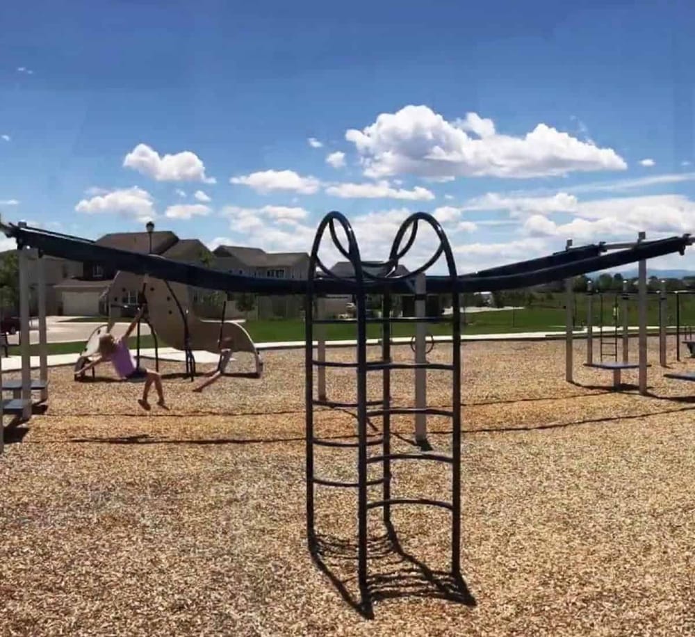 Colorful playground equipment with children playing outdoors under a bright, sunny sky in a residential neighborhood.