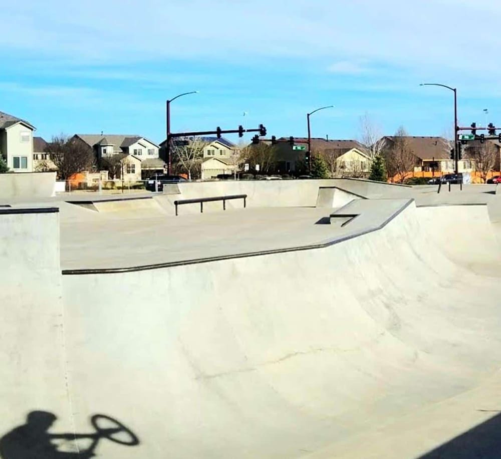 Empty concrete skatepark ramps with residential neighborhood in background, outdoor skateboarding recreational area, QuestForDirections site.