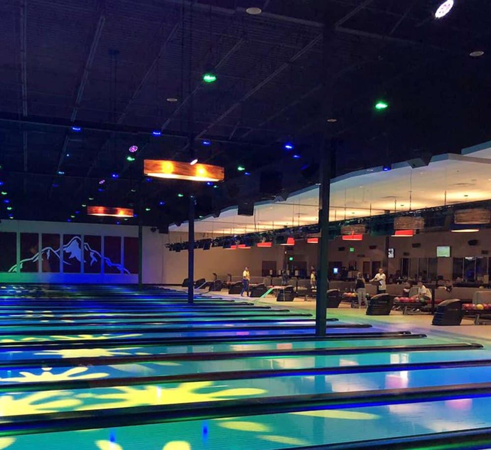Brightly lit upscale bowling alley with neon lights, seating area, and lanes for entertainment and social gatherings.