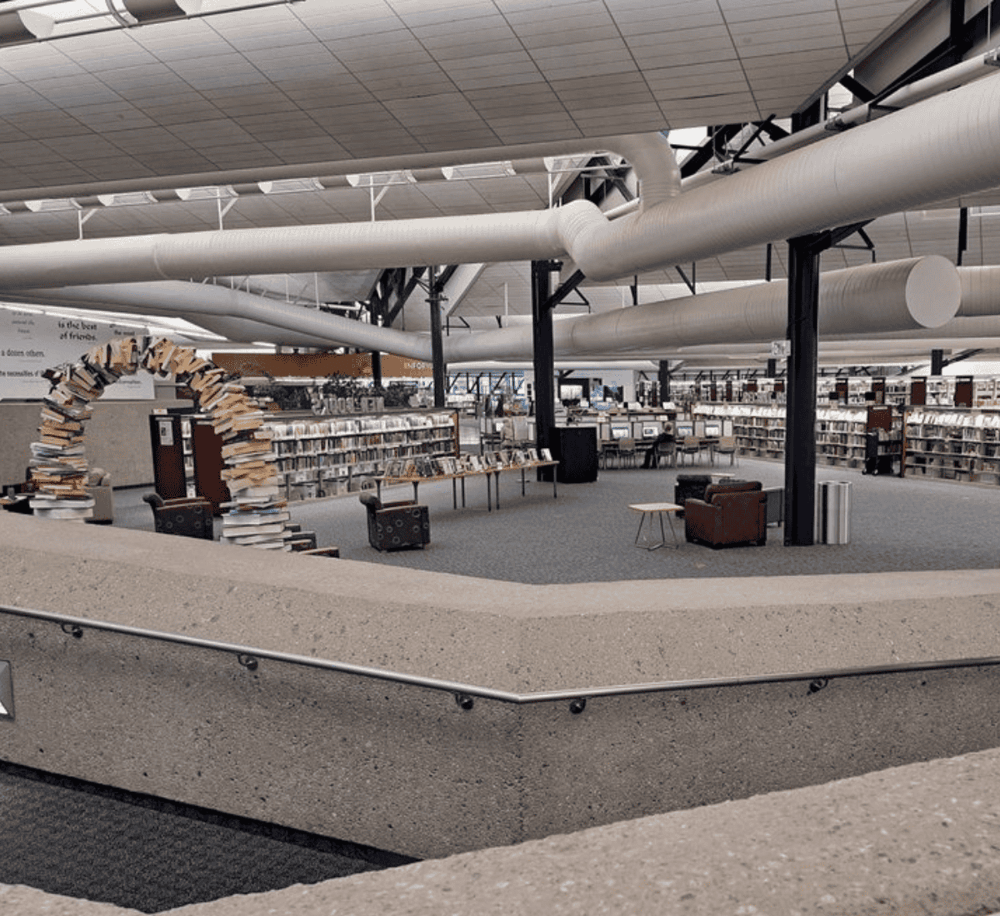 Stacks of books in a modern library interior with industrial design elements and curved ceiling ducts.