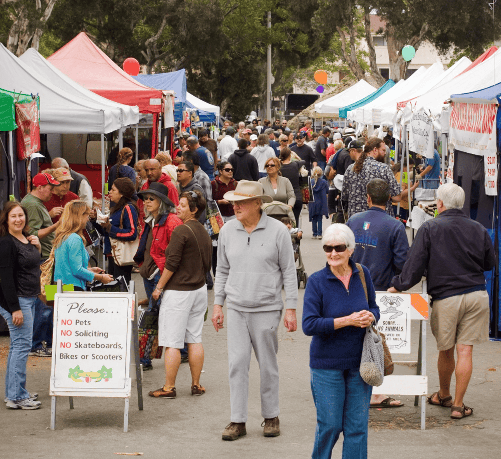 Colorful outdoor marketplace with diverse crowd and vendor tents.