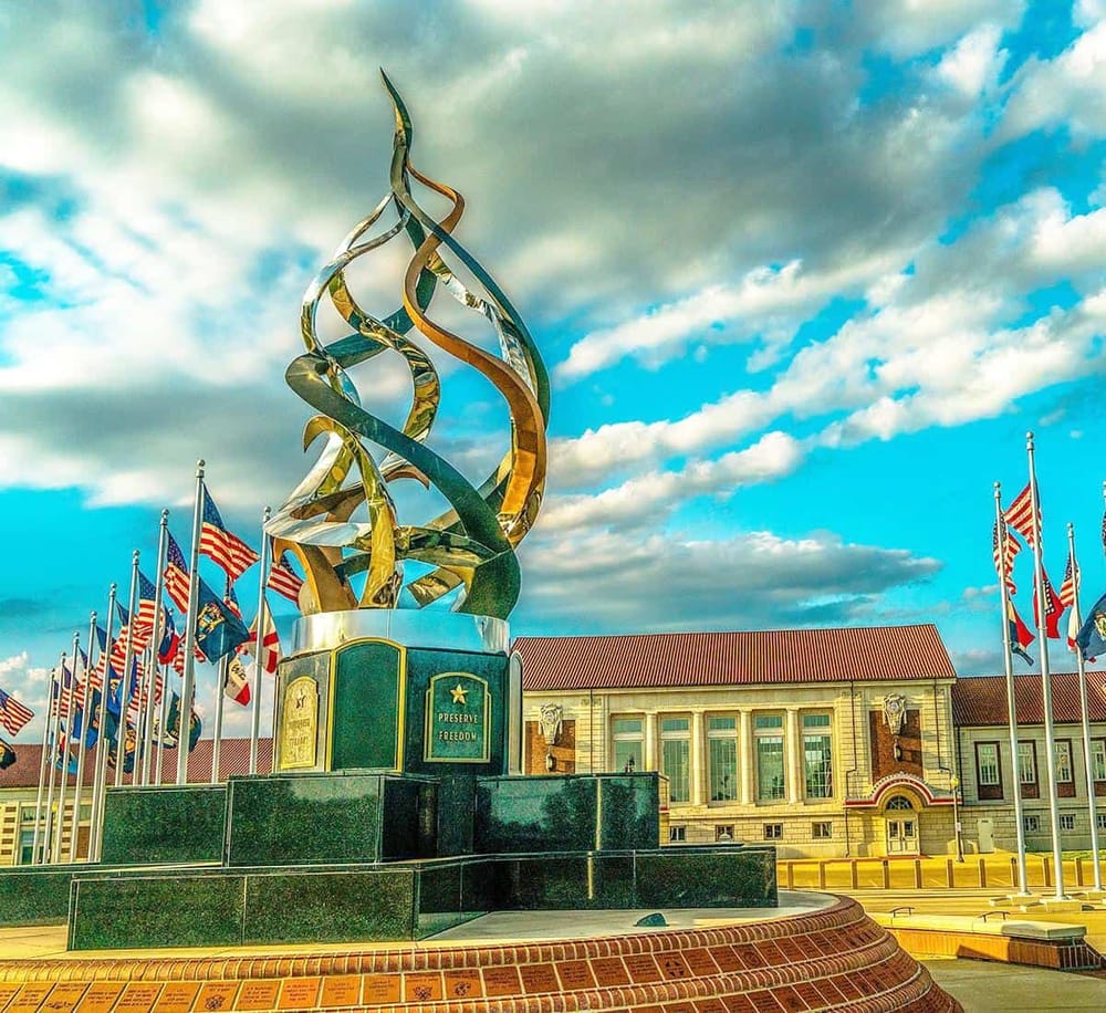 Bold, abstract sculpture with American flags, symbolizing freedom and patriotism. Located outside a historic building under a cloudy sky.