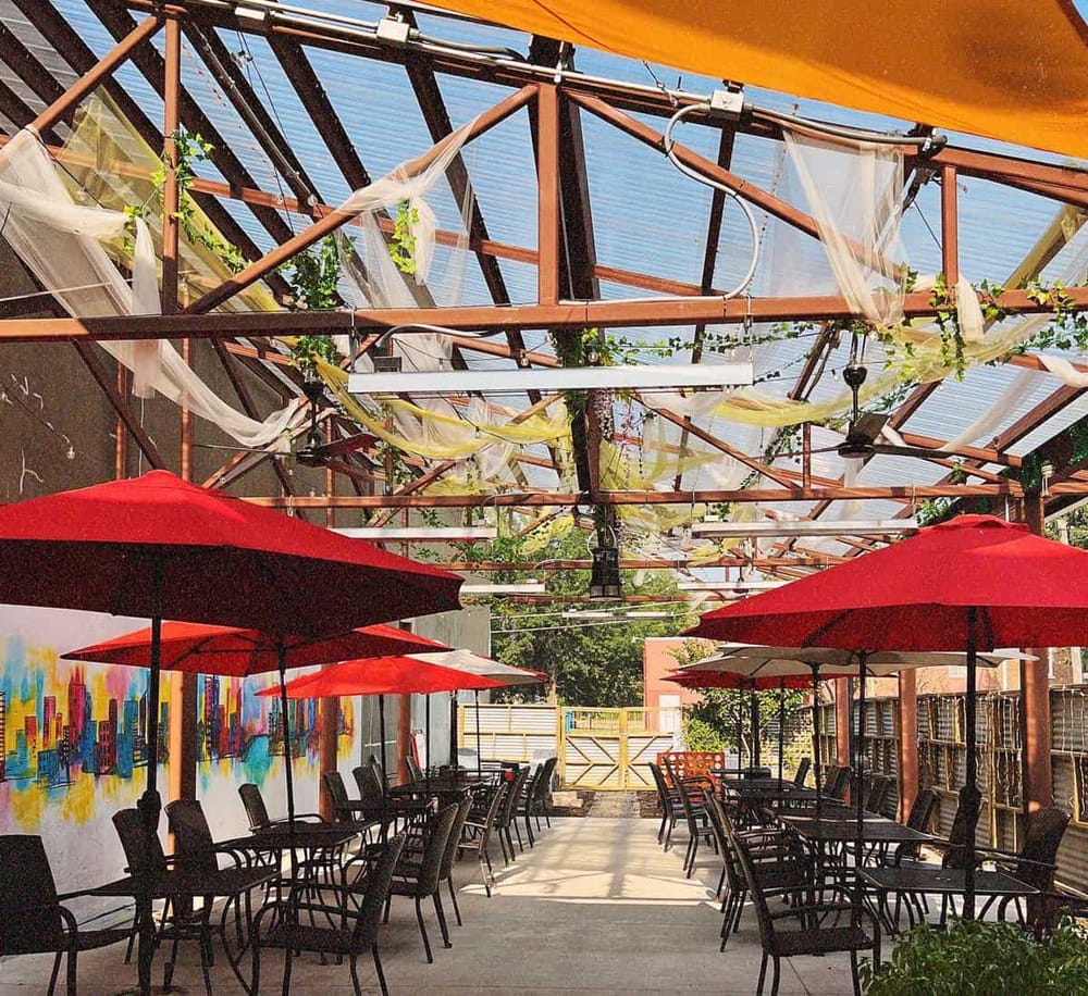 Colorful outdoor patio with red umbrellas and shaded pergola for dining and socializing.