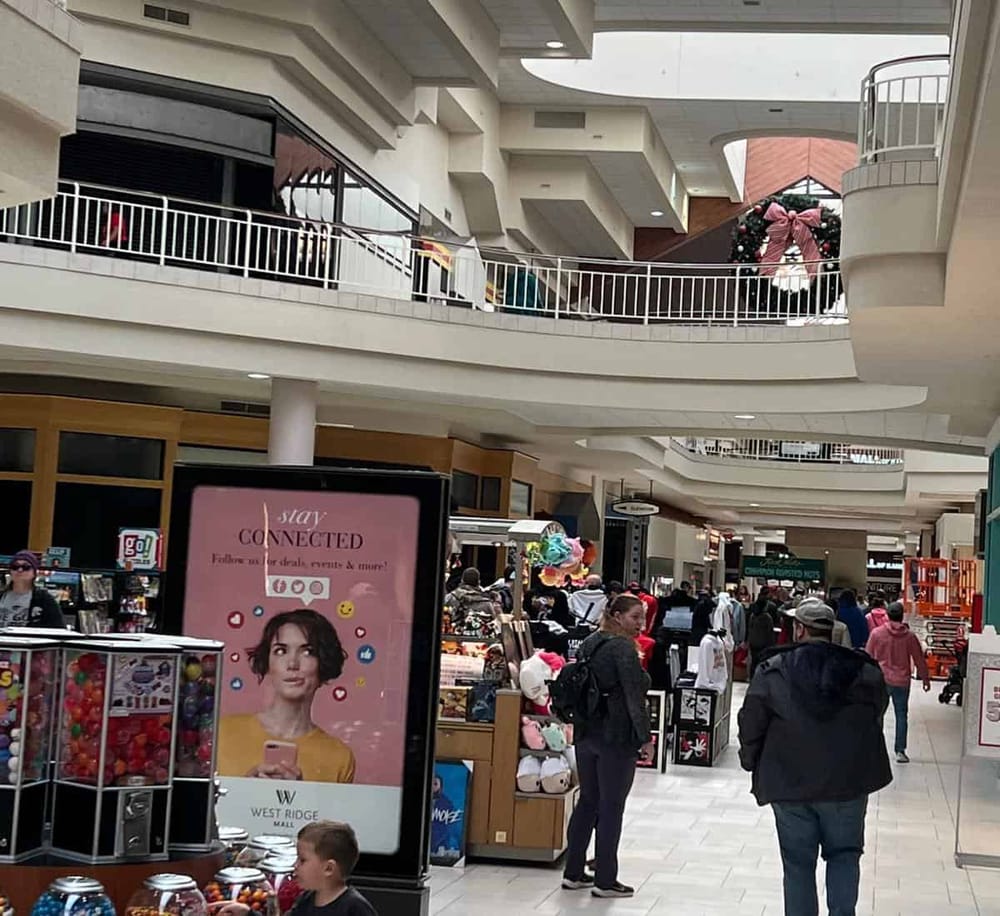 Bright indoor shopping mall with multiple levels, stores, holiday decorations, and shoppers at Quest for Directions.
