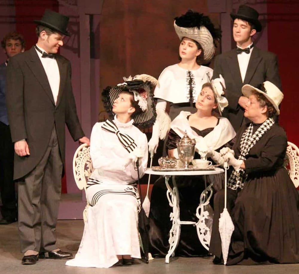 Elegant Victorian-era setting featuring actors in period costumes, showcasing classic theater performance scenes.