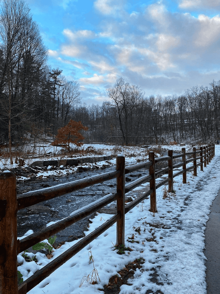 Snow-covered trail with wooden fence along a wintery river scene.