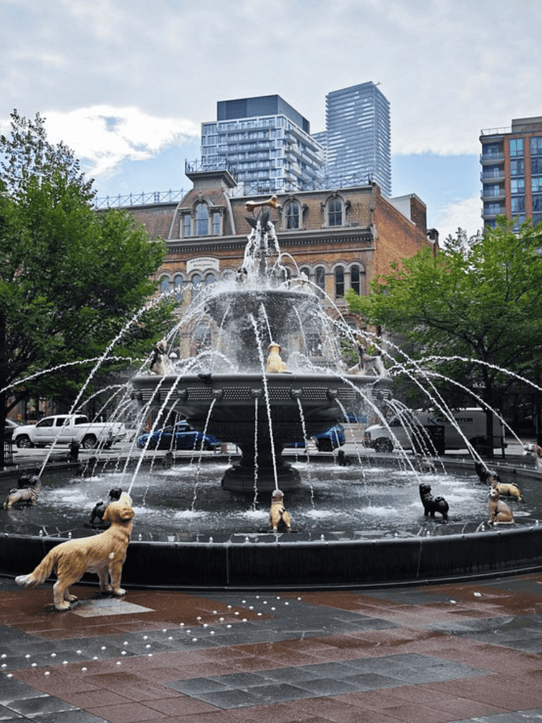 Colorful Fountain in Downtown City with Dog Statues and Modern Skyscrapers Nearby.