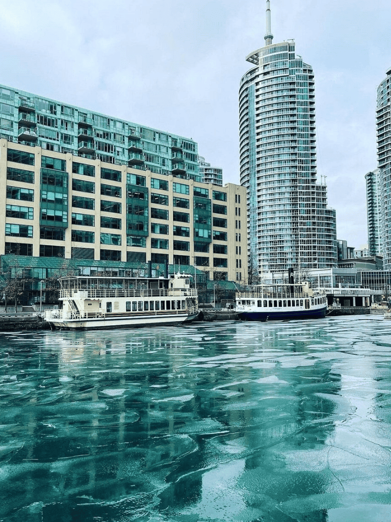 Modern cityscape with waterfront buildings and boats in a metropolitan harbor area.