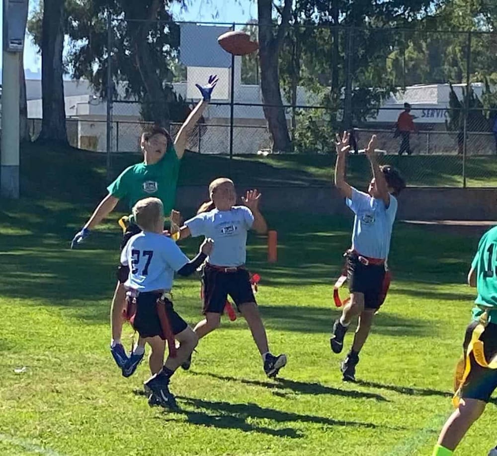 Children playing flag football during an outdoor game on a sunny day.