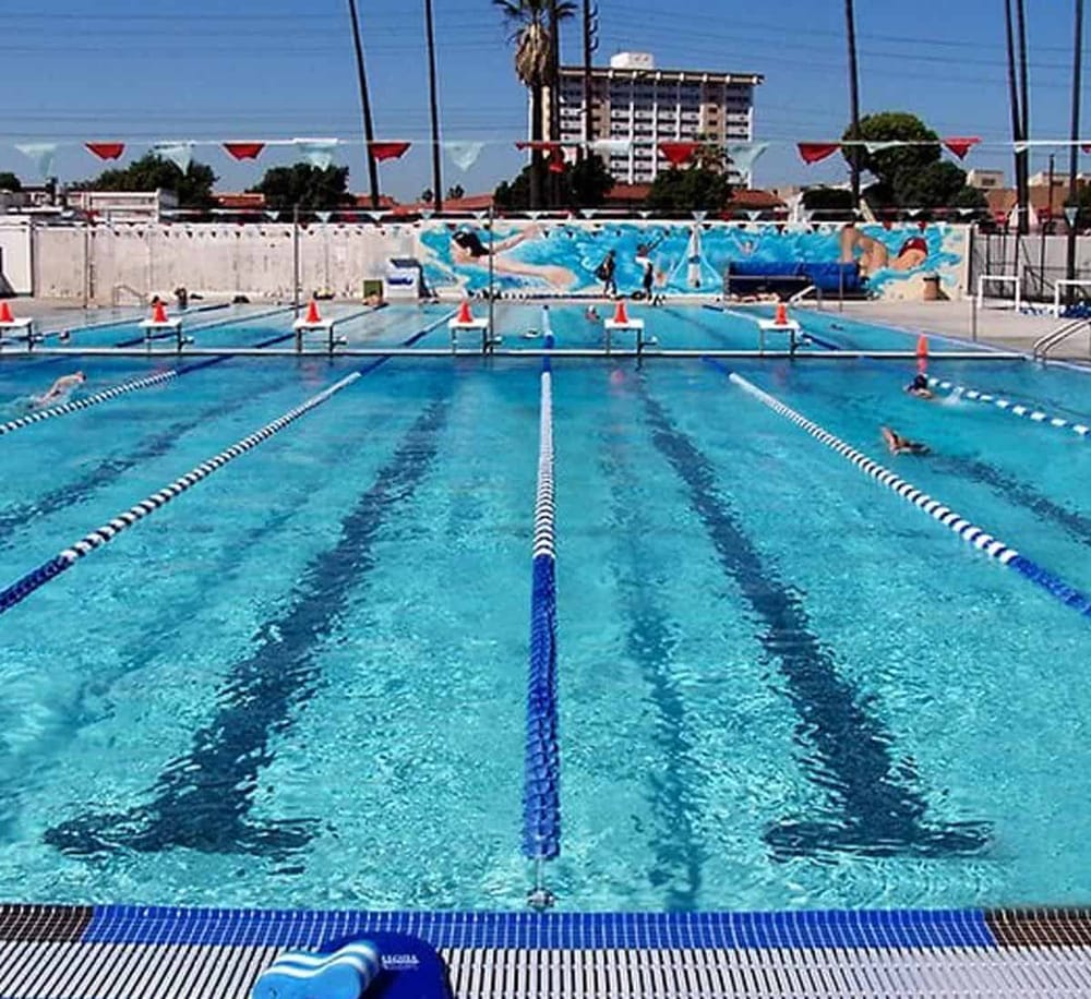 Kids swimming pool with lane markers and a colorful mural in the background, sunny outdoor sports facility.