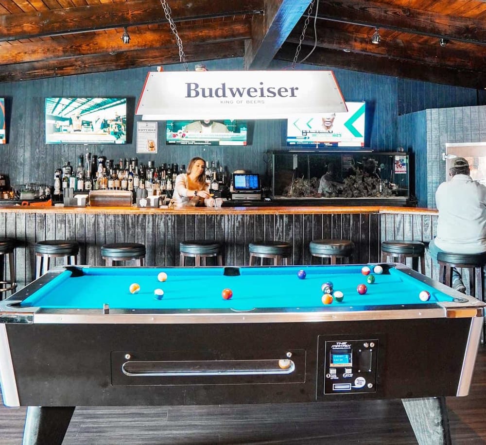 Bright billiards pool table at a bar with a Budweiser sign and televisions in the background.