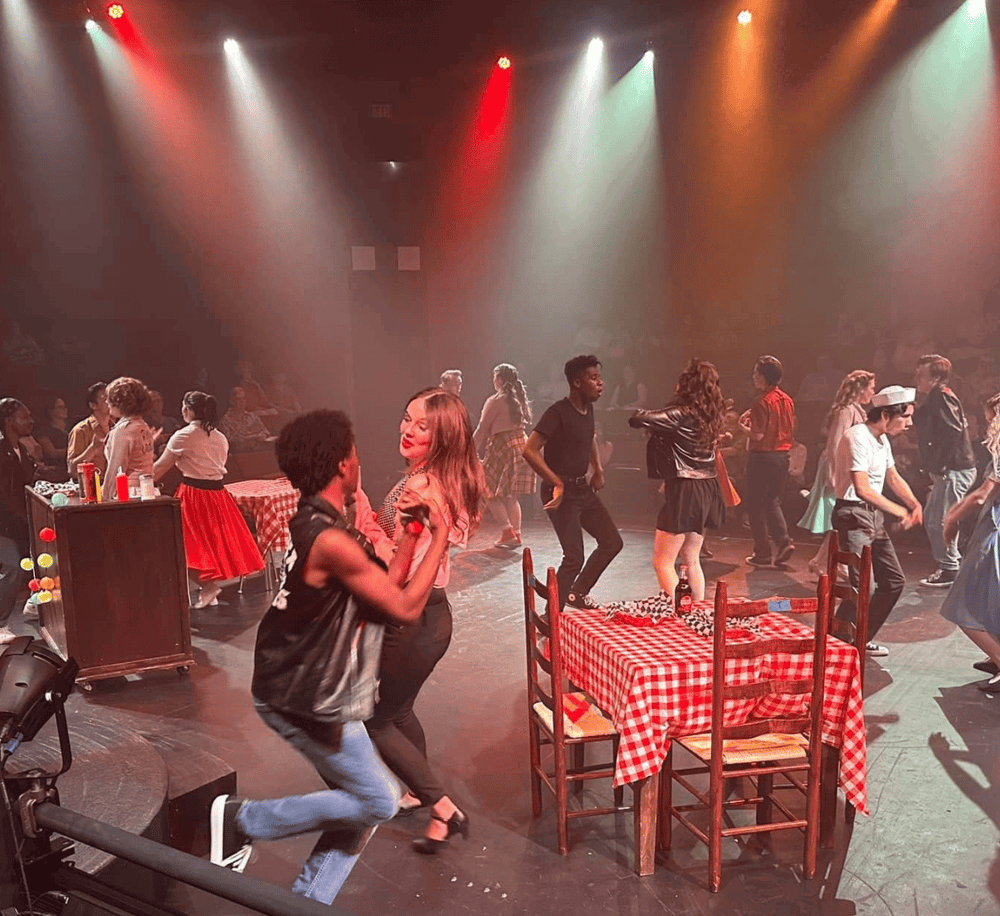 Dancing crowd on stage at a lively themed event with colorful lighting and retro decor.