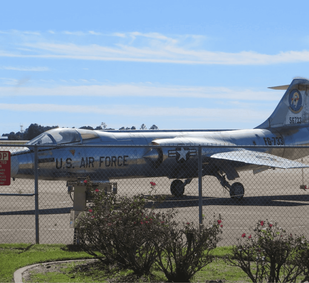 Vintage U.S. Air Force fighter jet parked at an airport, surrounded by a chain-link fence.