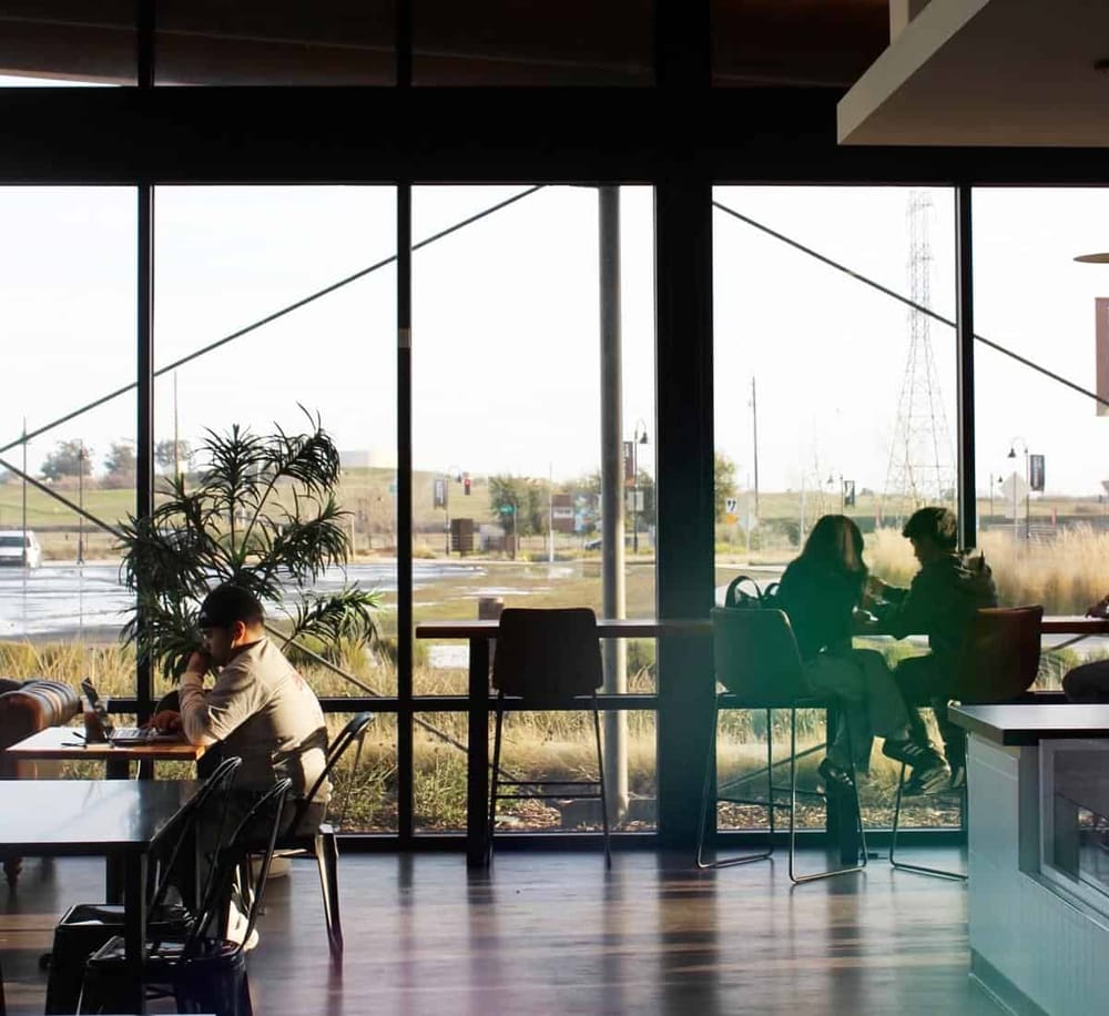 Cozy coffee shop interior with large window views, ideal for relaxing or remote work.