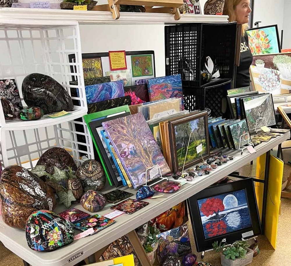 Colorful handcrafted art and painted rocks display at local art fair. Unique home décor and art pieces for sale. Visit QuestForDirections for art inspiration.
