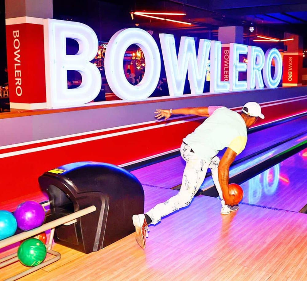Colorful neon lights at Bowlero bowling alley with person playing and colorful bowling balls.