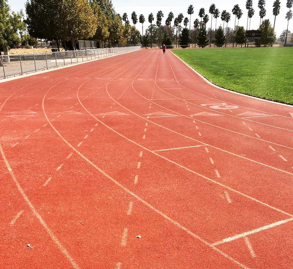 Running track at a sports complex with multiple lanes and green field on side, ideal for athletic training and outdoor exercise.