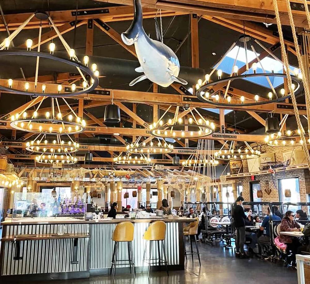 Brightly lit restaurant interior with wooden beams, hanging chandeliers, and a mounted fish decoration.