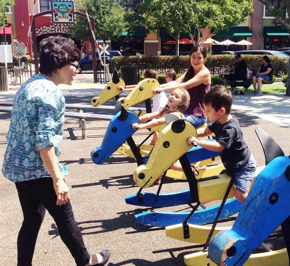 Colorful kids' ride-on animals at a park playground, with smiling children and an adult supervising.