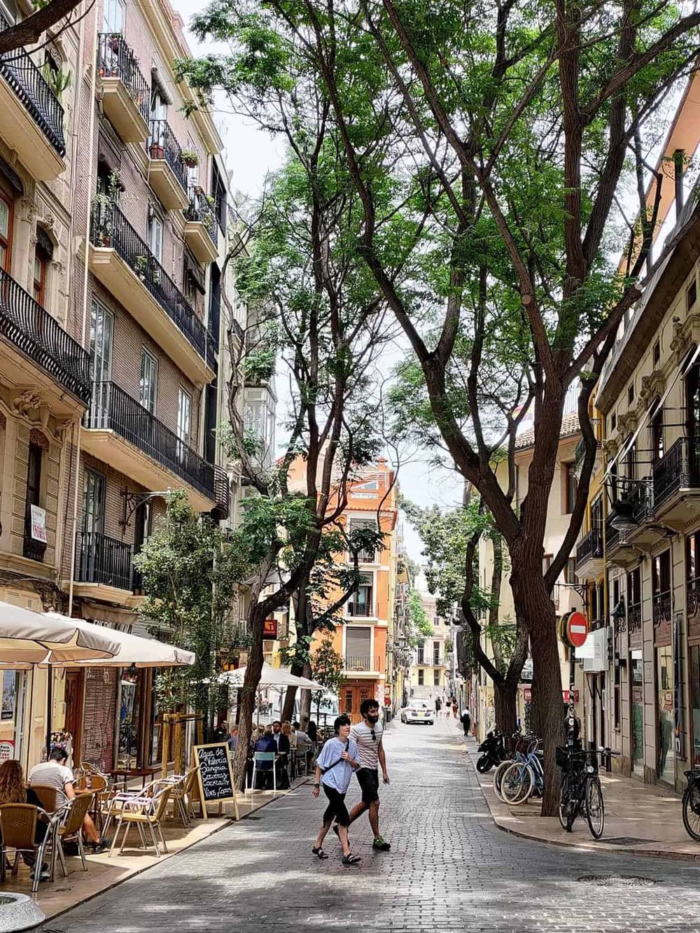 Bustling city street with outdoor cafes, tall buildings, and green trees, perfect for urban exploration and local dining.