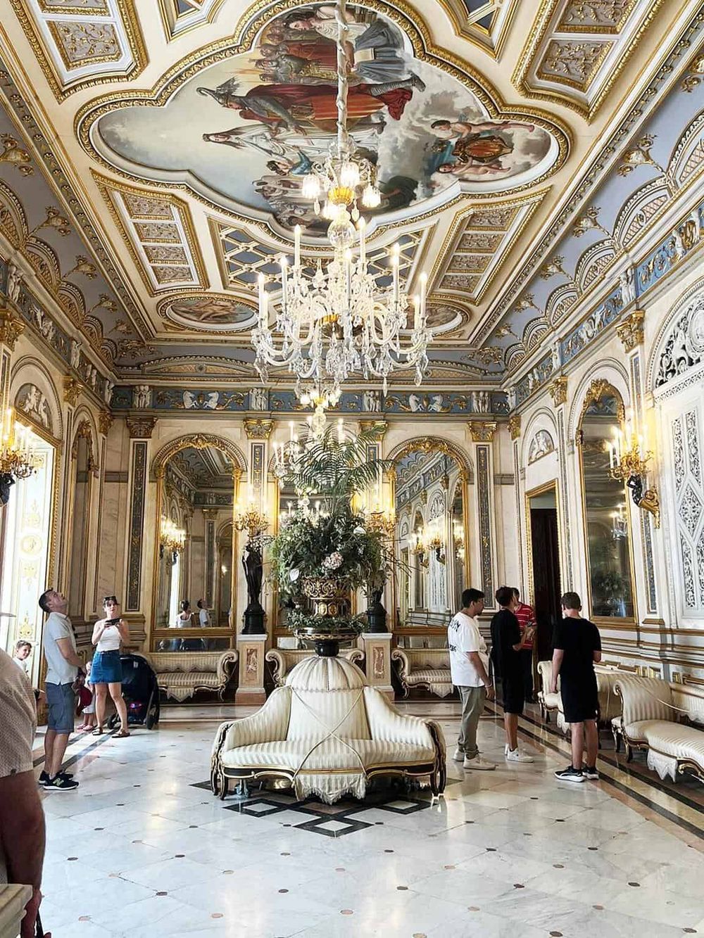 Elegant palace interior with ornate gold accents and a grand chandelier, showcasing luxury and historical architecture.