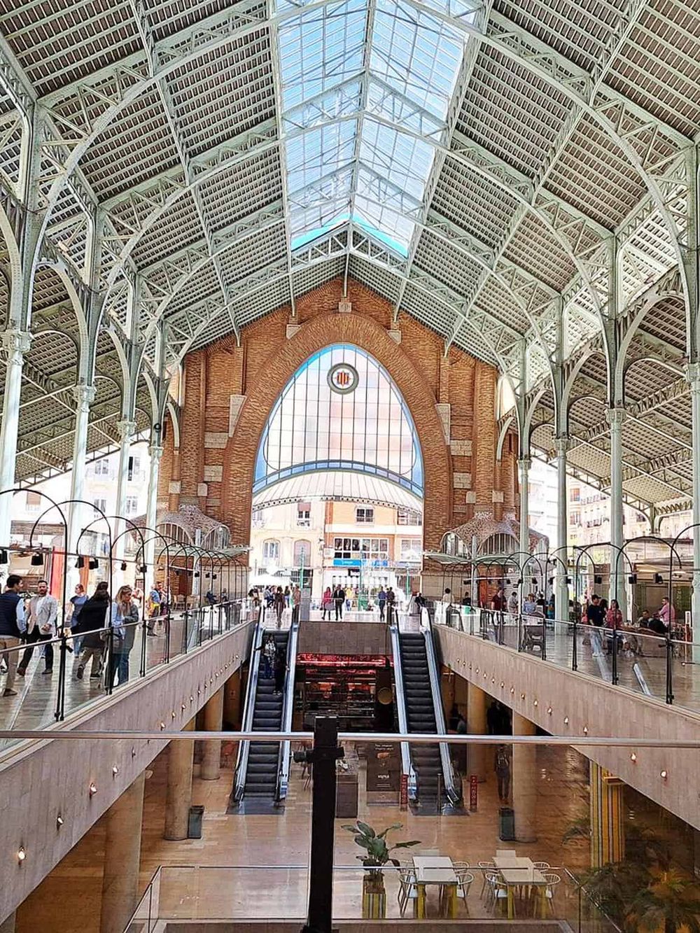 Bright indoor shopping mall with historic architecture and skylight, showcasing diverse retail stores and bustling shoppers.