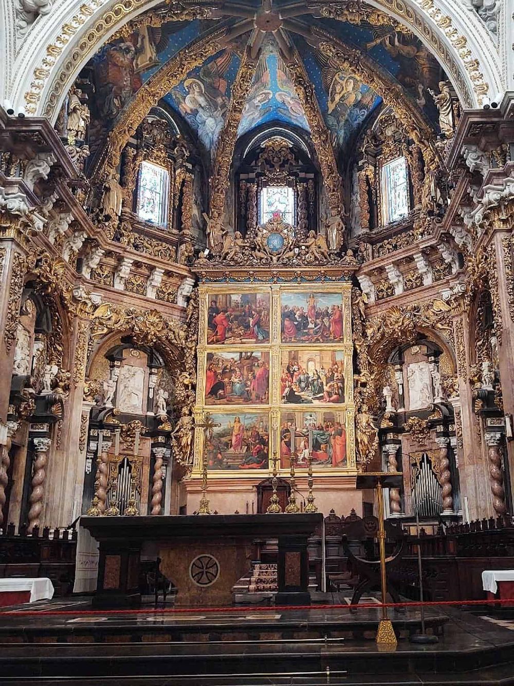 Intricate Baroque church altar with gold detailing, religious paintings, and ornate stucco architecture.