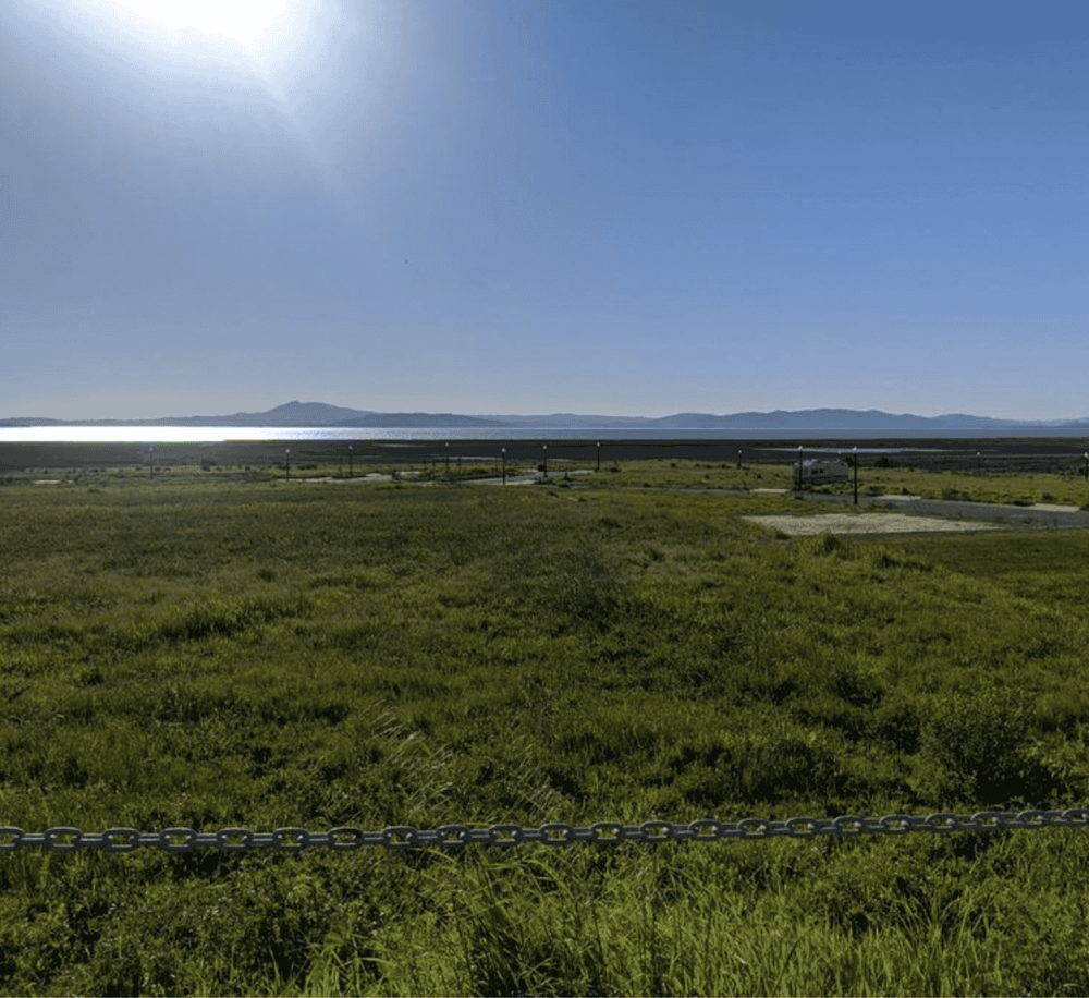 Serene landscape with open green field, distant mountains, and bright sunny sky for travel and outdoor adventures.