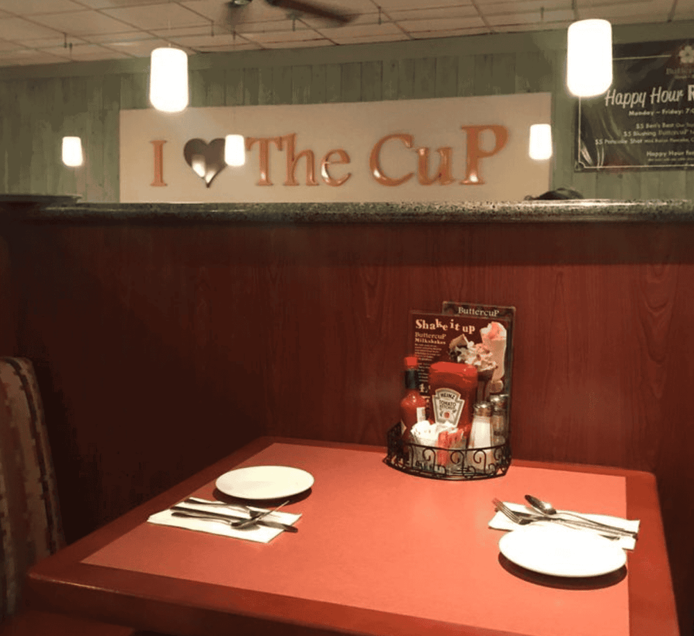 Freshly set table at cozy restaurant with "I Love The Cup" sign in background, ideal for breakfast or lunch.