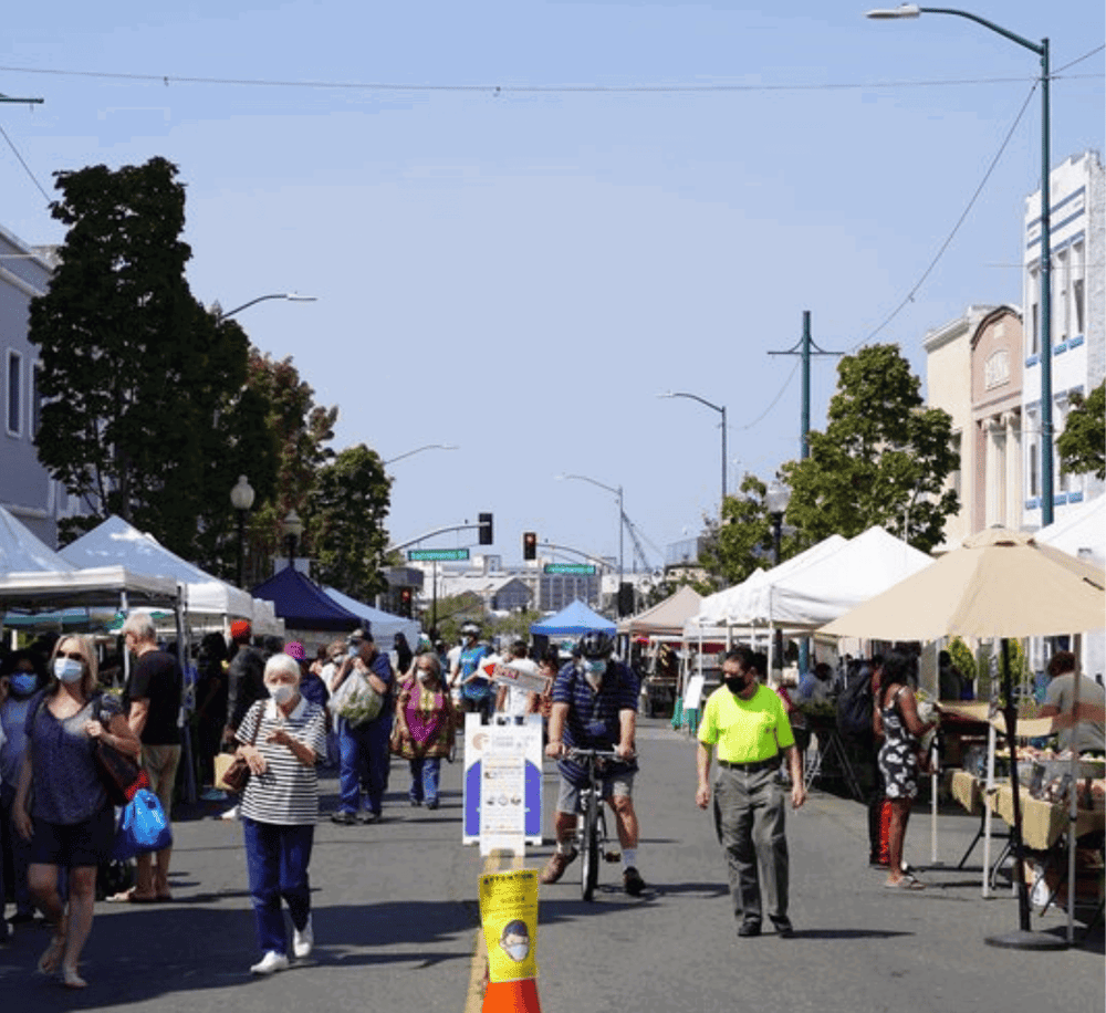Local outdoor marketplace at QuestForDirections, vibrant street fair with vendors, shoppers, and social distancing, supporting local businesses.