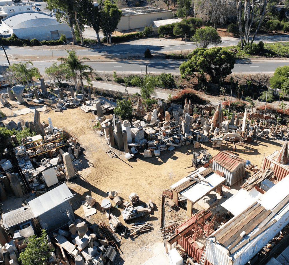 Old stone yard with sculptures, construction materials, and storage sheds in an outdoor workshop.