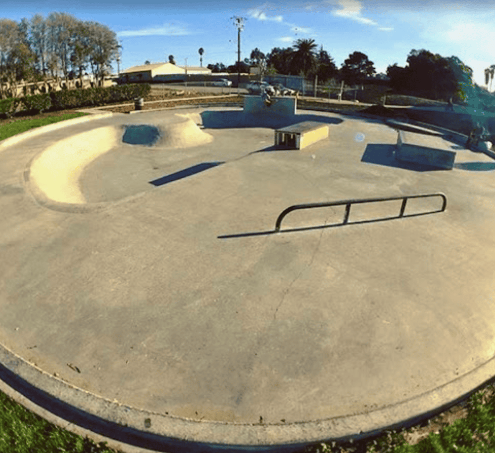Aerial view of a skatepark with ramps, rails, and a bowl for skating and BMX riding, sunny outdoor setting.