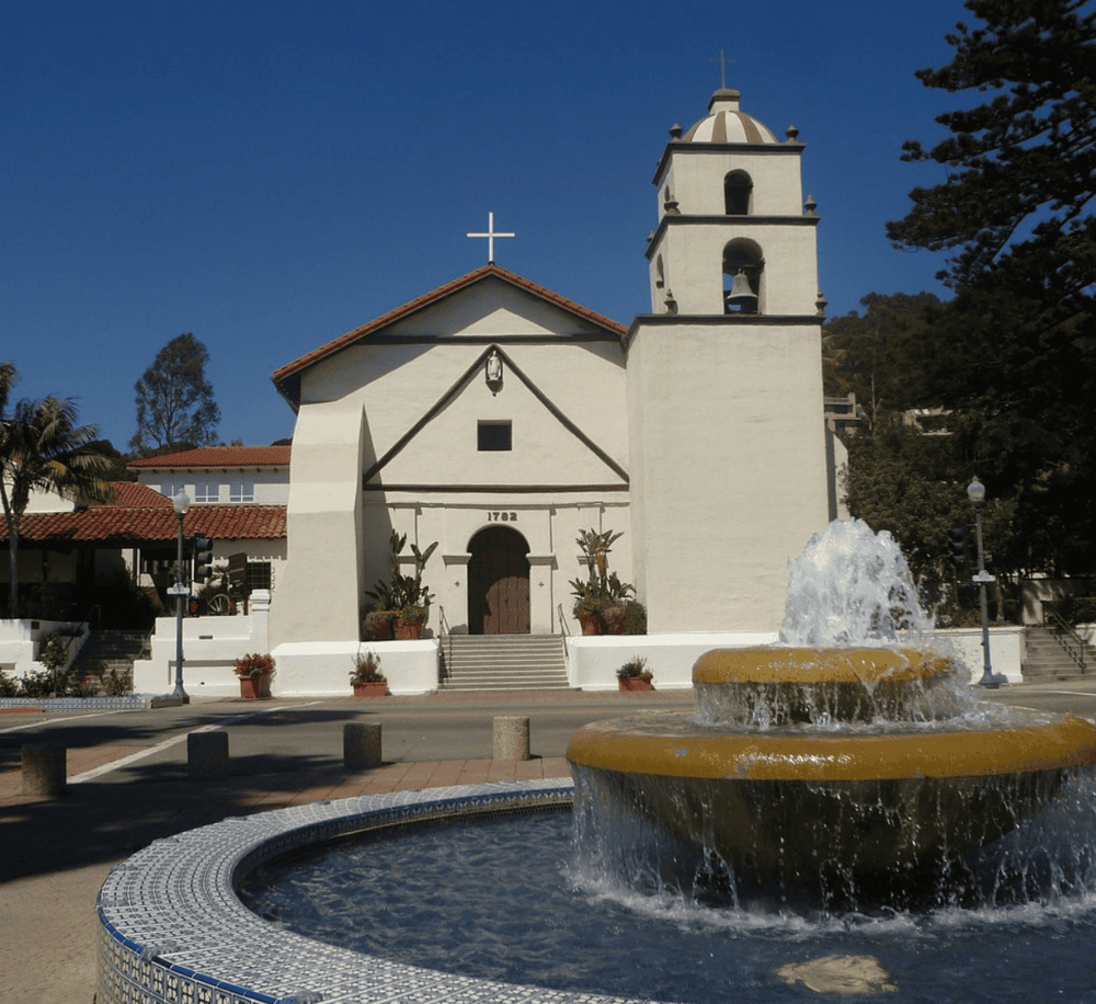 Historic Mission Church San Juan Capistrano with fountain and blue sky.